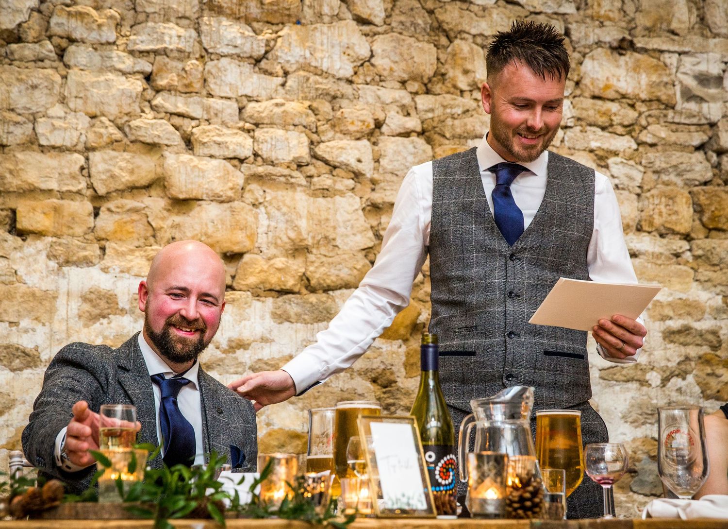 Wedding reception speeches and toasts against stone wall backdrop at rustic venue.