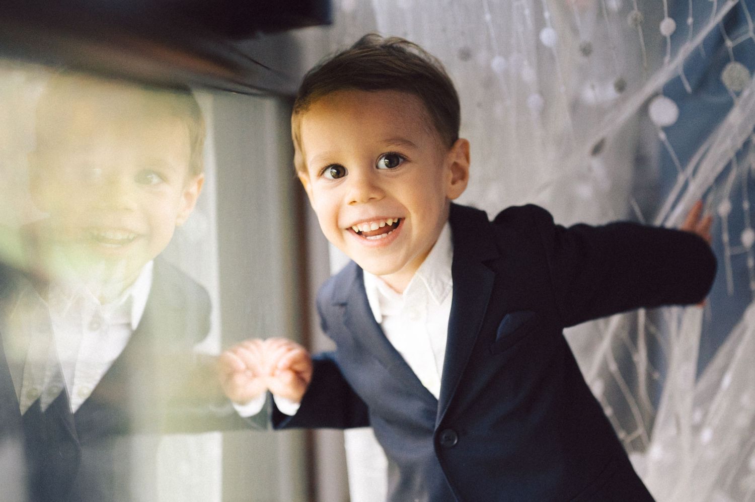 A child in formal wear smiles brightly while playing near a window.