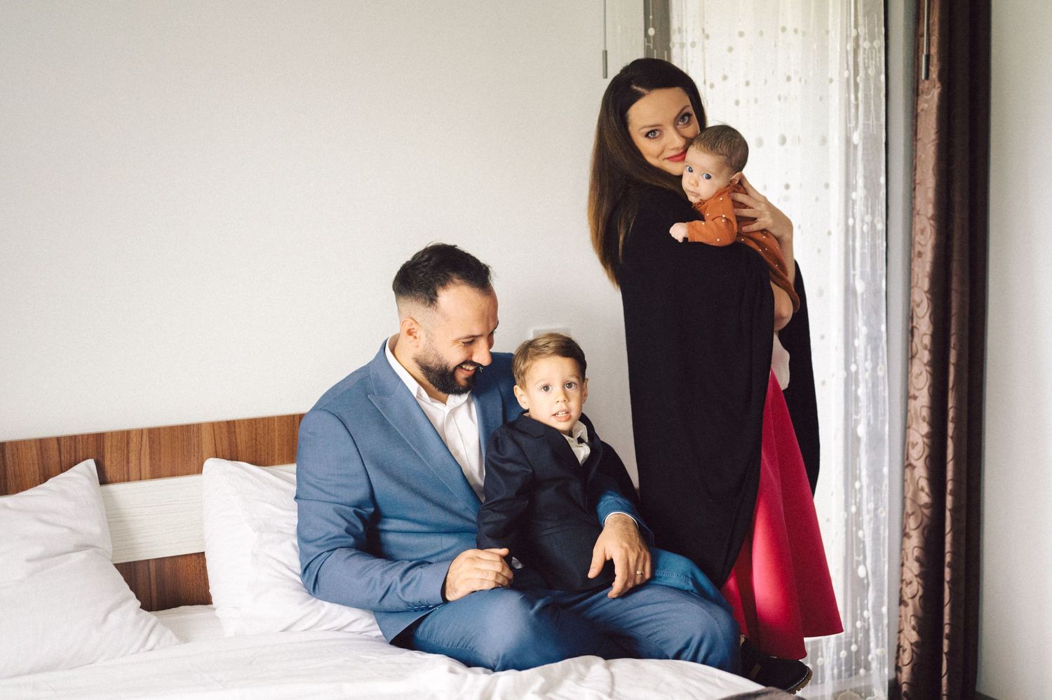Family relaxing together on a white bed in a sunlit room.
