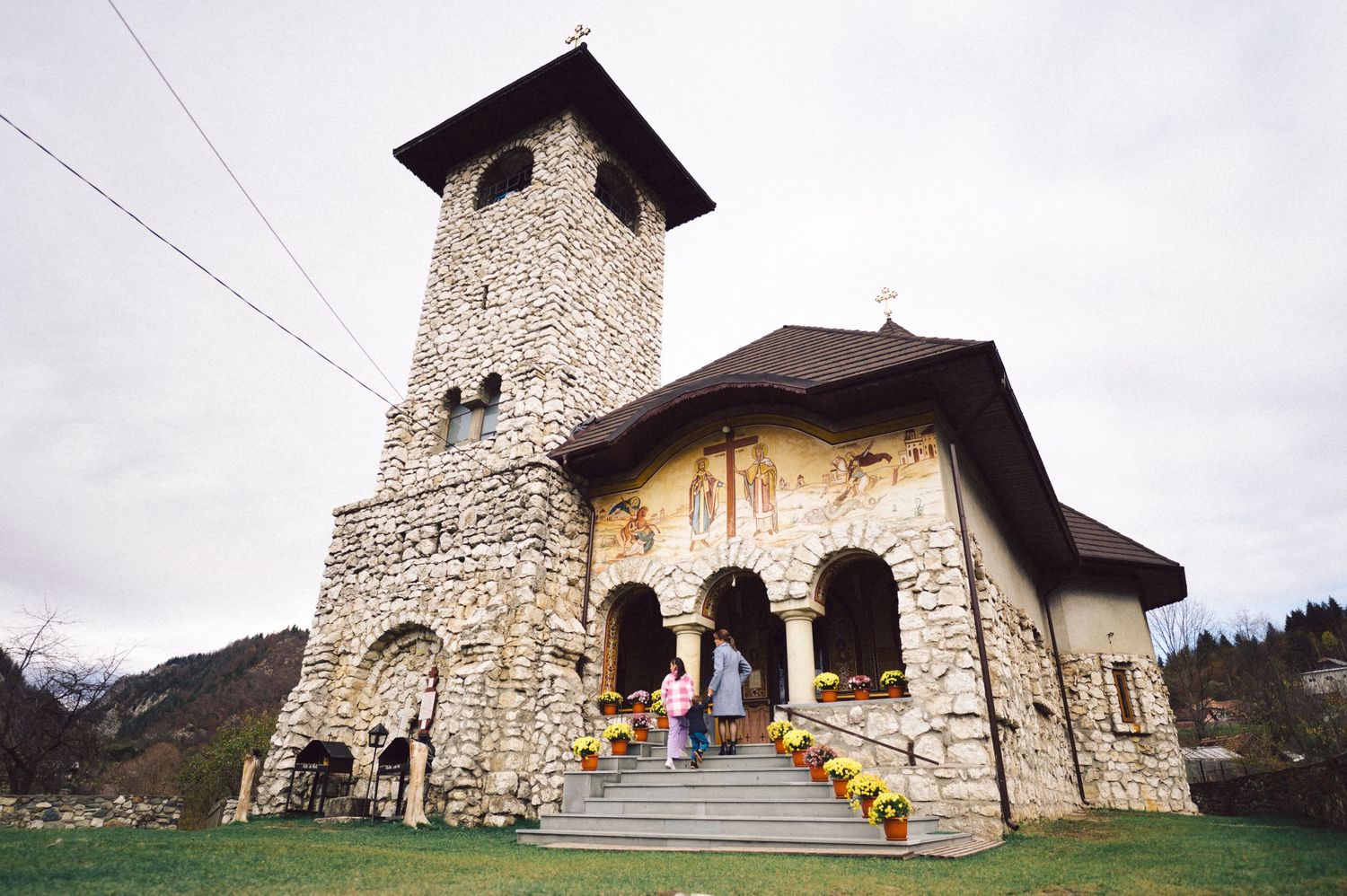 Stone church with bell tower and decorated entrance stairs against cloudy sky.
