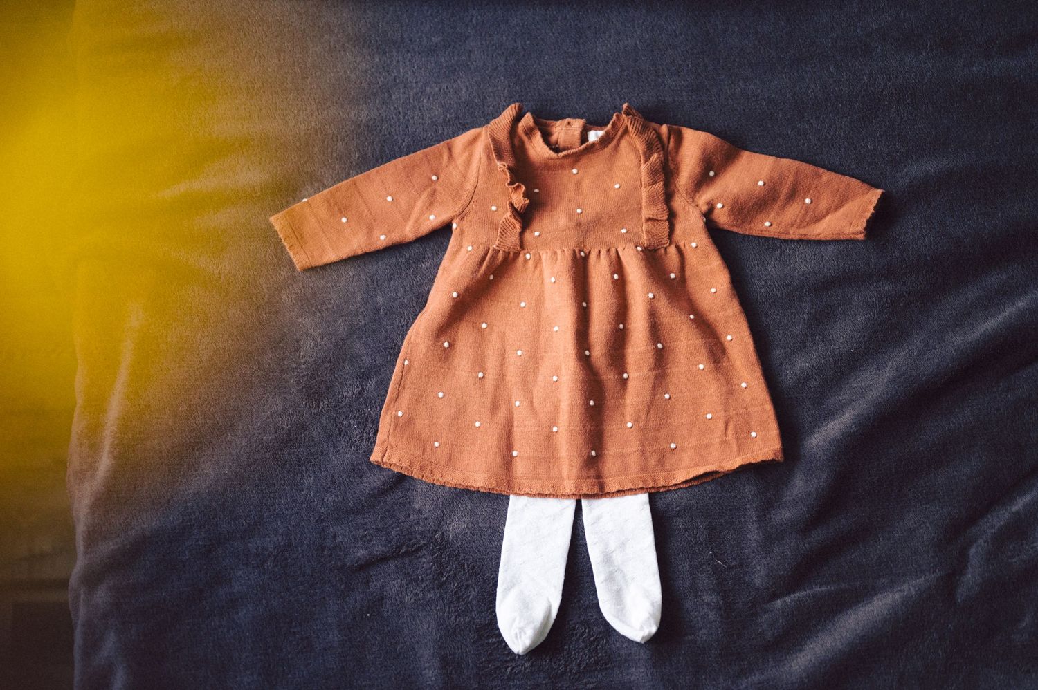 Small orange dress with white tights laid flat against dark background with warm lighting.