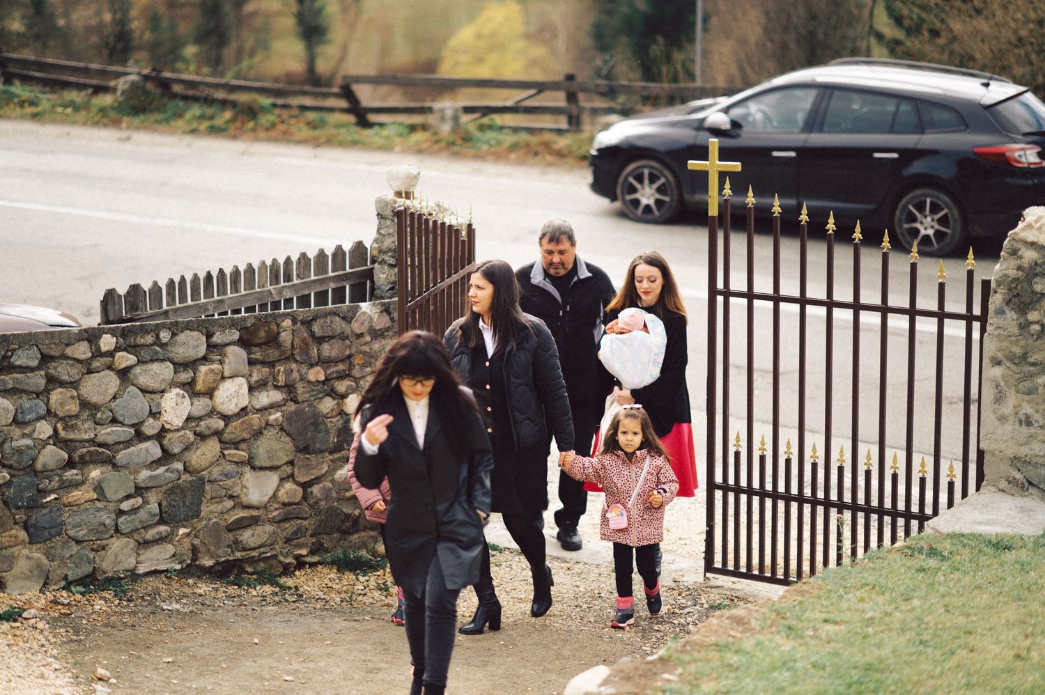 Group of people walking through iron gates of stone wall enclosure.