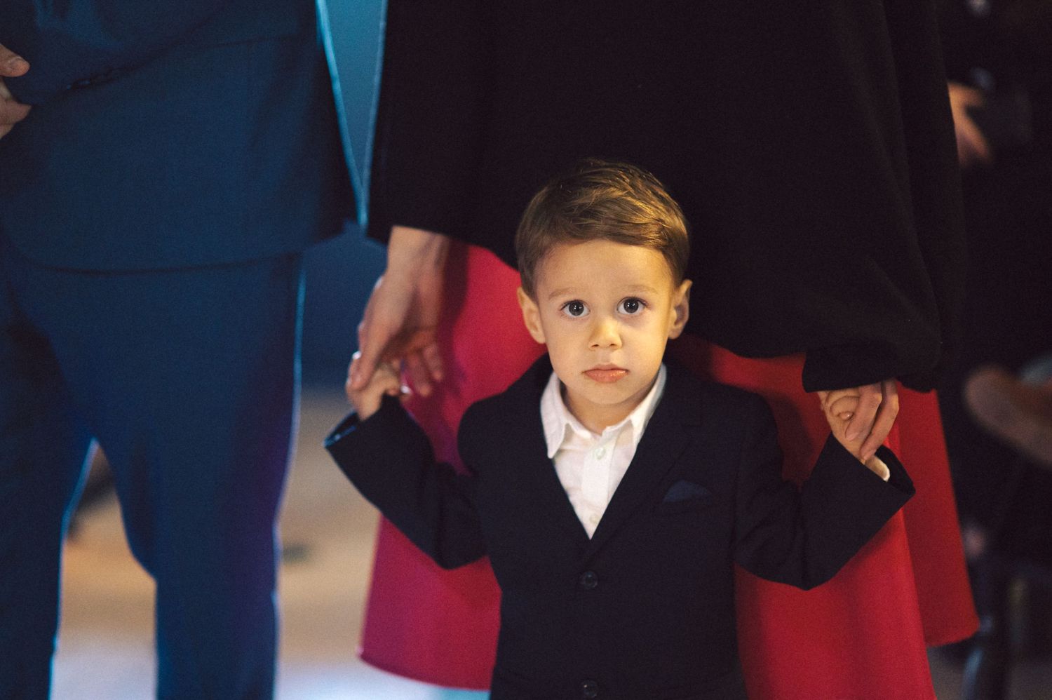 Young child in formal navy suit standing in church during ceremony.