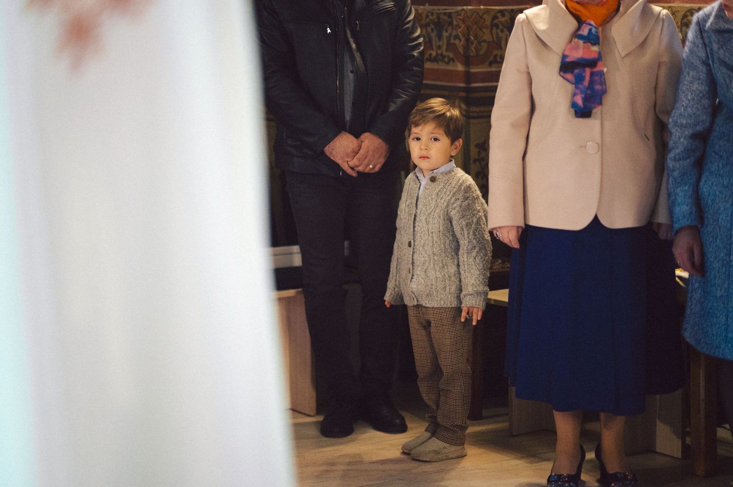 Child in gray sweater standing during formal church ceremony.