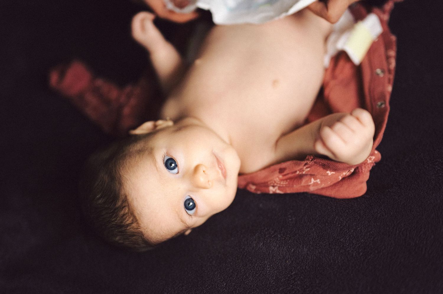 Small infant lying on dark fabric wearing coral colored clothing.