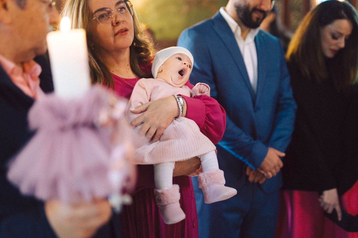 A baby dressed in pink being held during a christening ceremony at church.