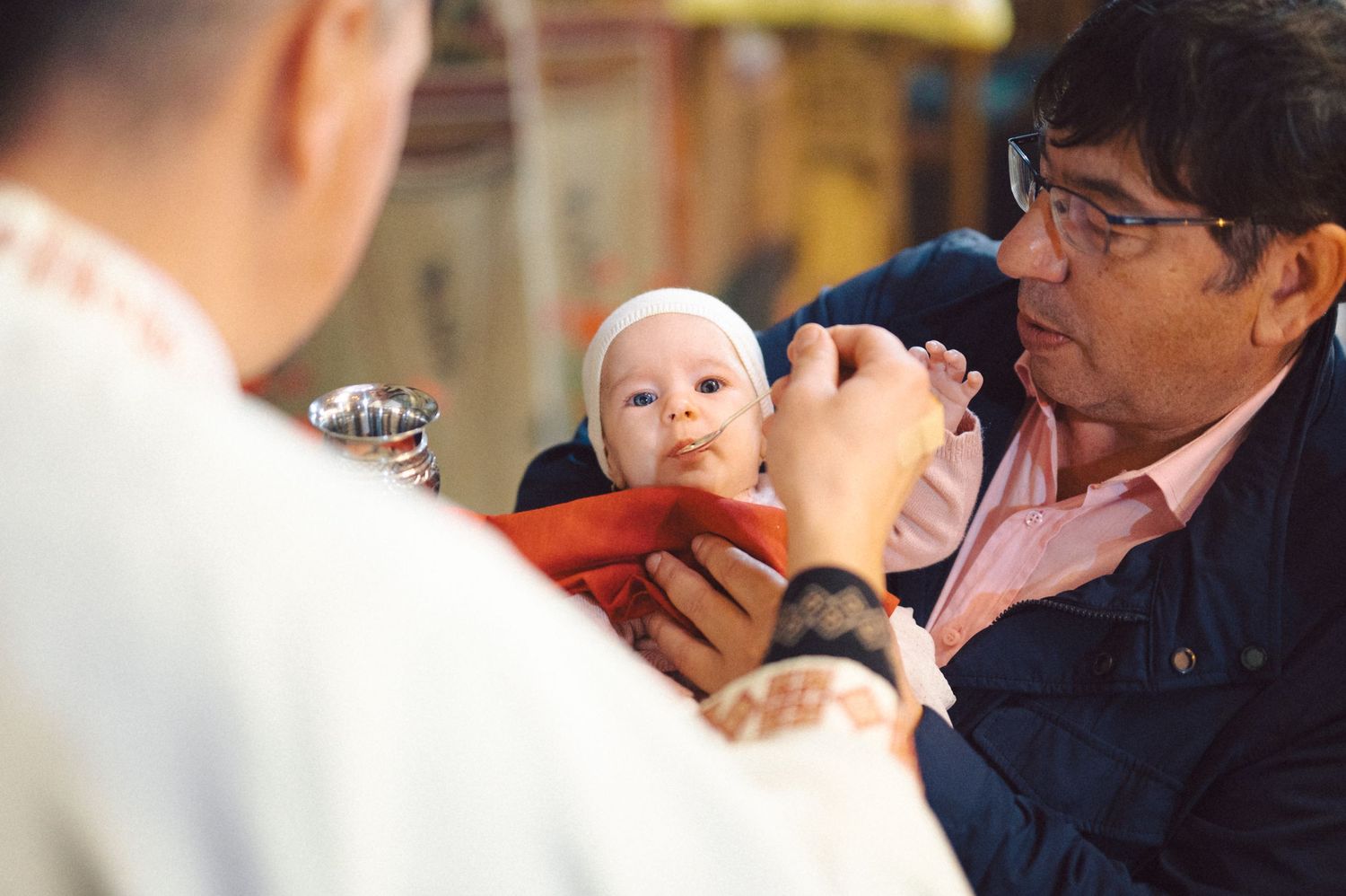 A baby being held during a religious ceremony with attendees watching.