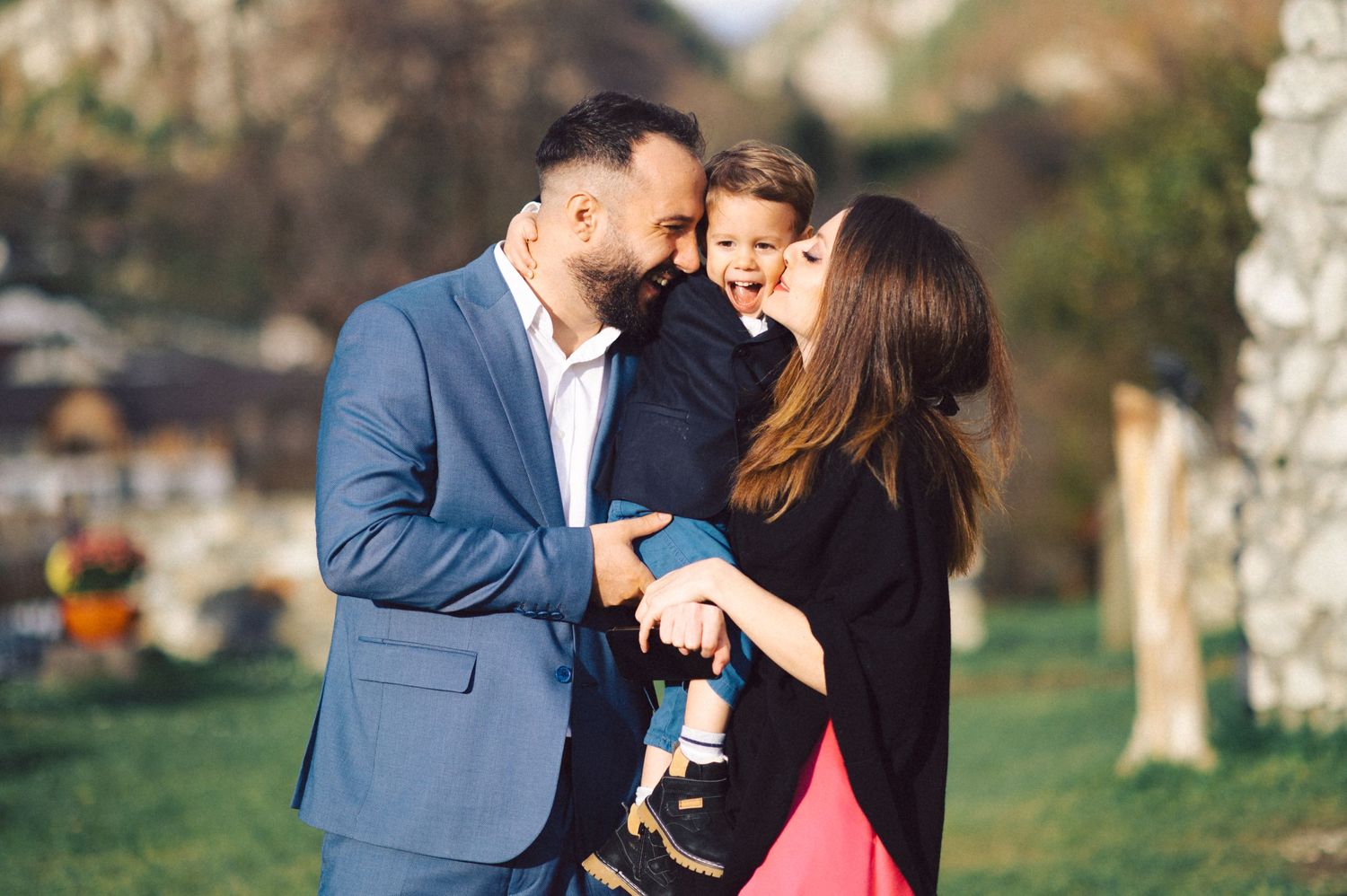 A tender family moment captured outdoors in a park on a sunny day.