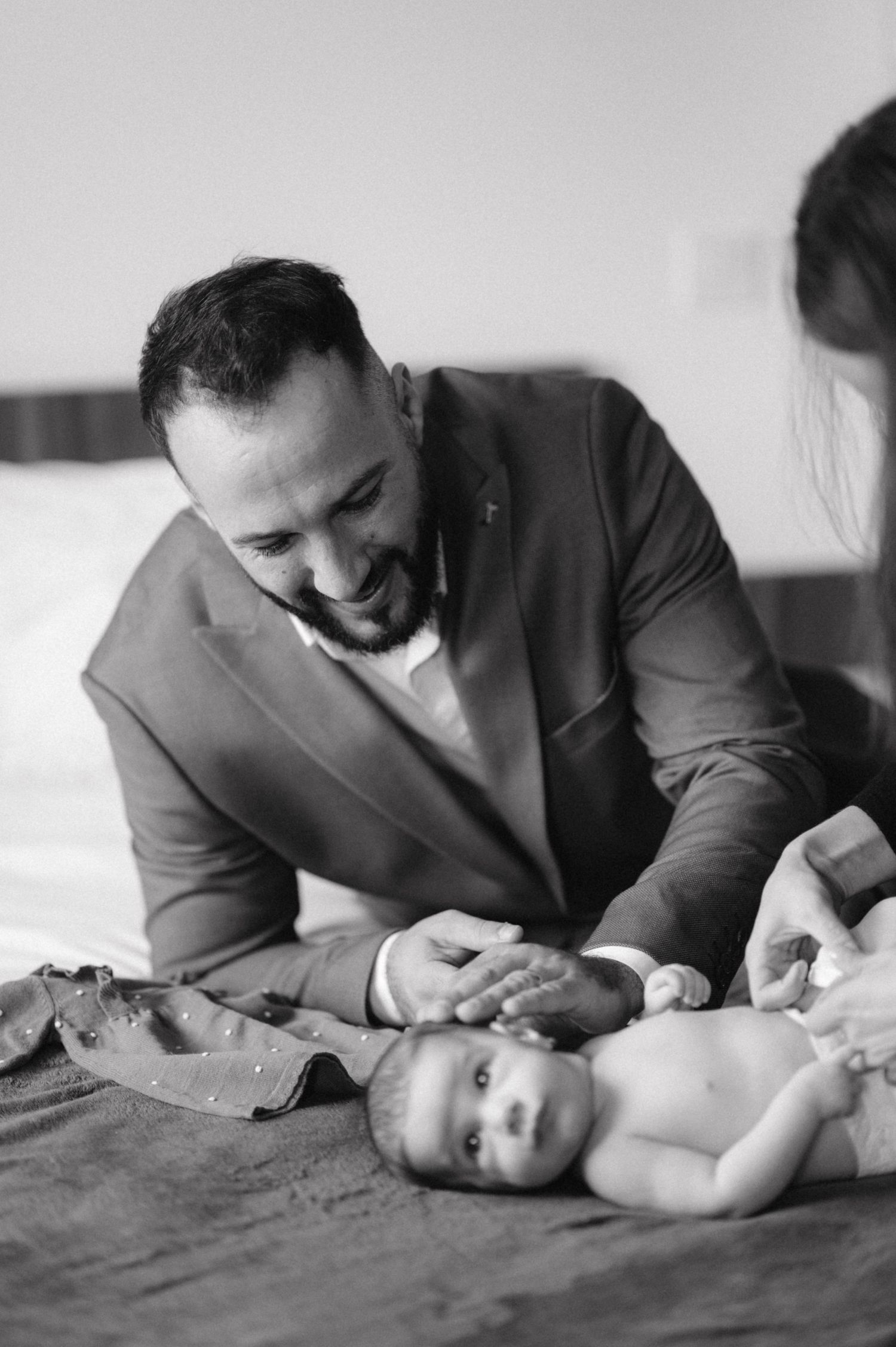 Tender parenting moment as adults interact with infant on dark bedding.