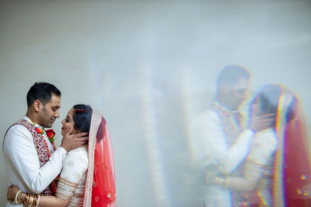 A romantic couple in traditional Indian wedding attire shares an intimate moment against a light background.