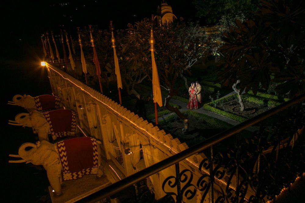 An ornate balcony overlooks a garden at night with illuminated pillars and railings.