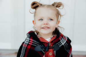 Child wearing a plaid winter scarf and red outfit against white background.