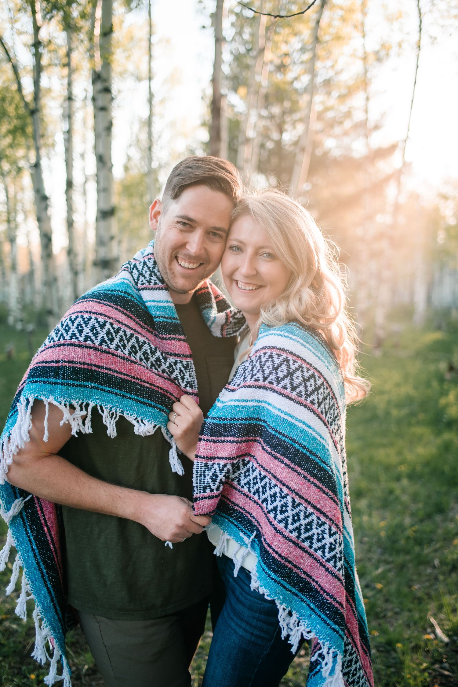 Couple sharing blanket and laughter in sunlit aspen grove.