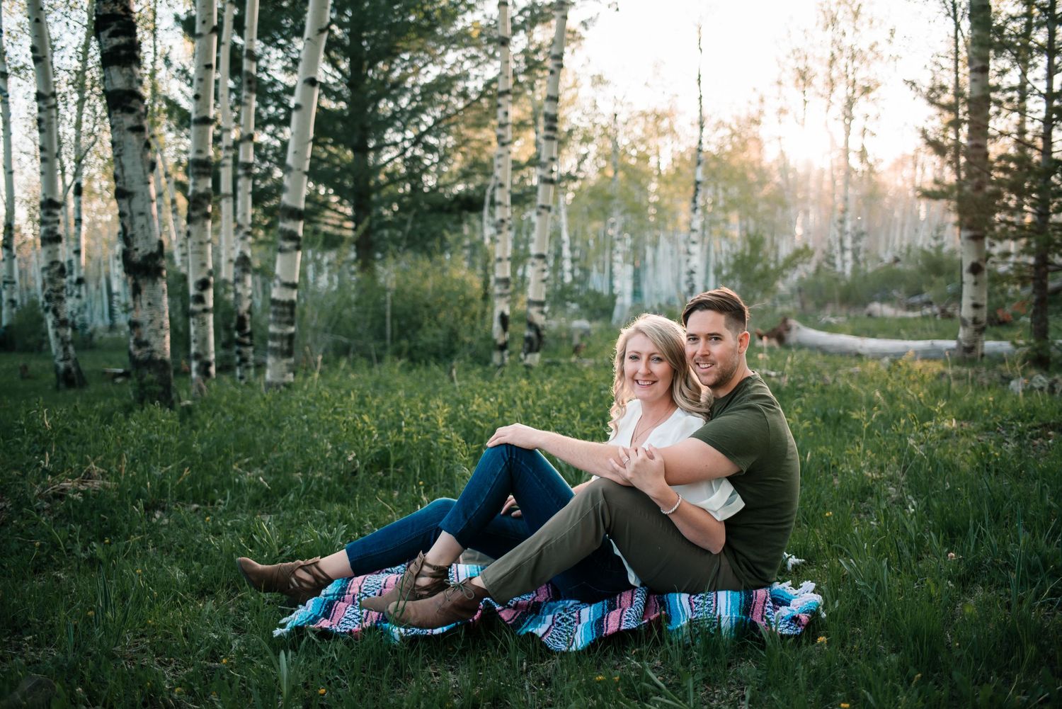 Couple shares tender moment in a sunlit aspen grove while wrapped in a colorful striped blanket.