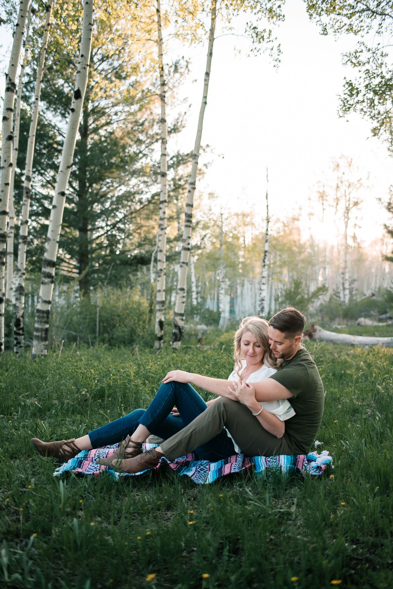 Playful couple relaxing on patterned blanket among aspen trees at sunset.