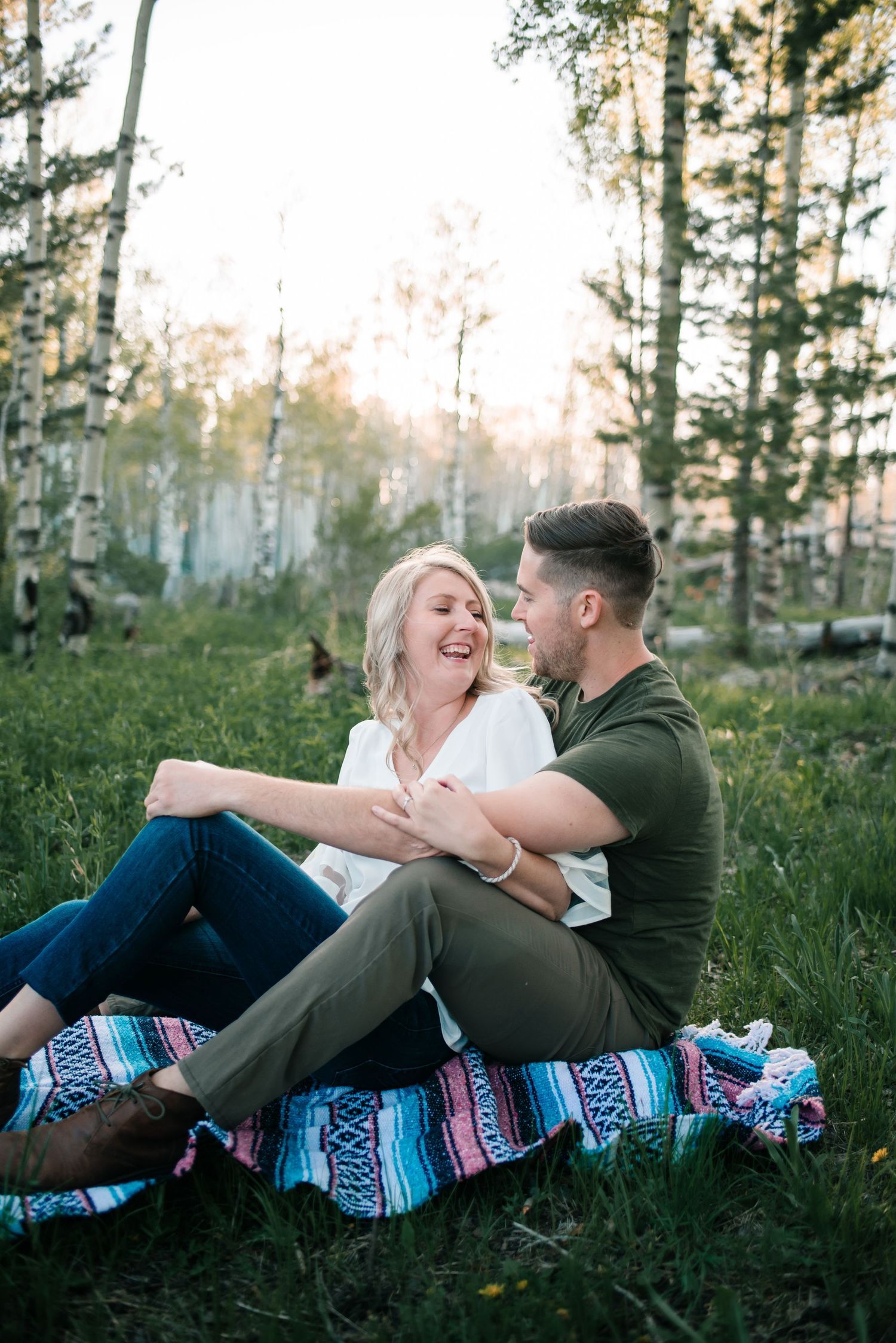Couple lying on blanket in aspen forest during golden hour photography session.