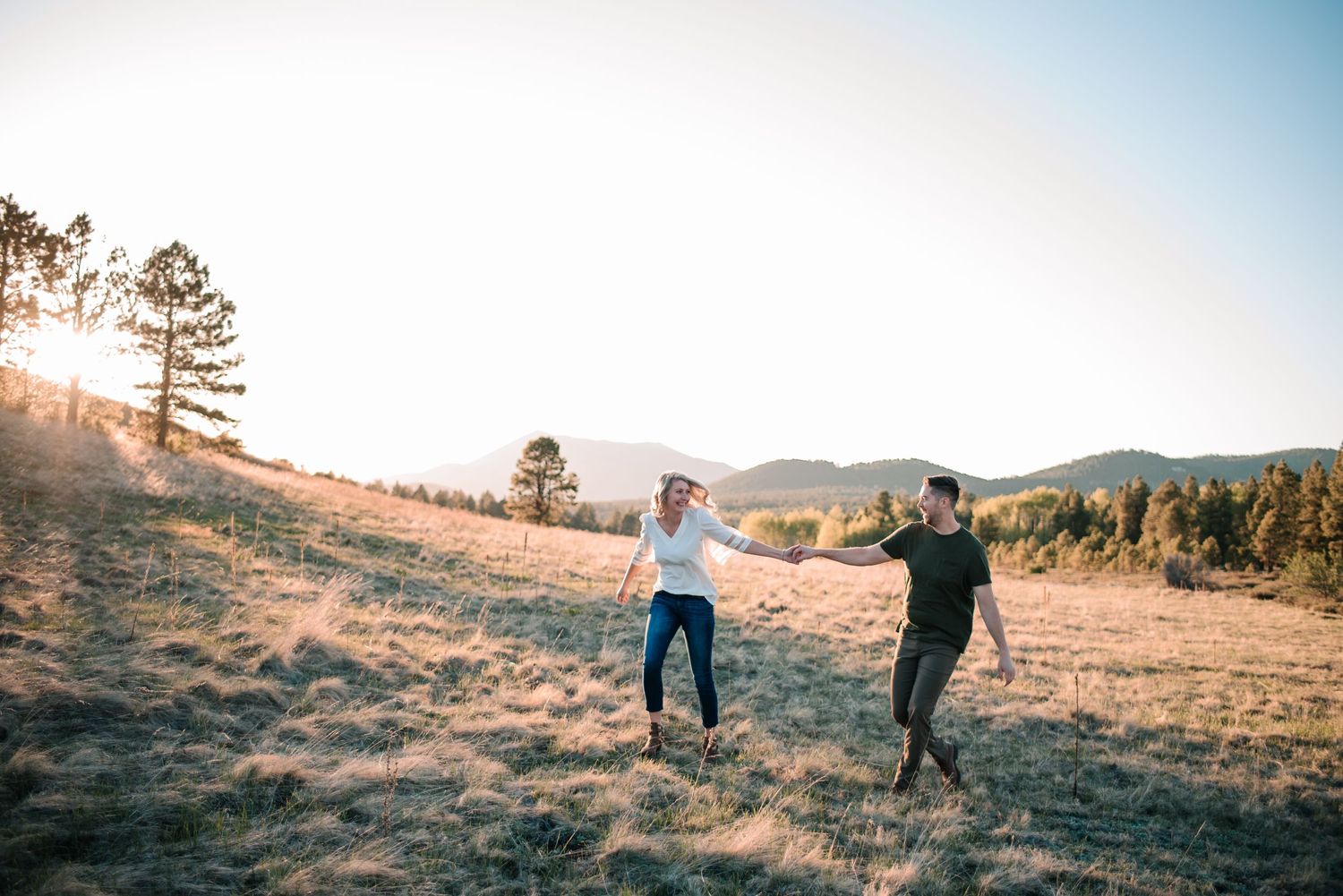 Two people walk hand in hand across a scenic mountain landscape.