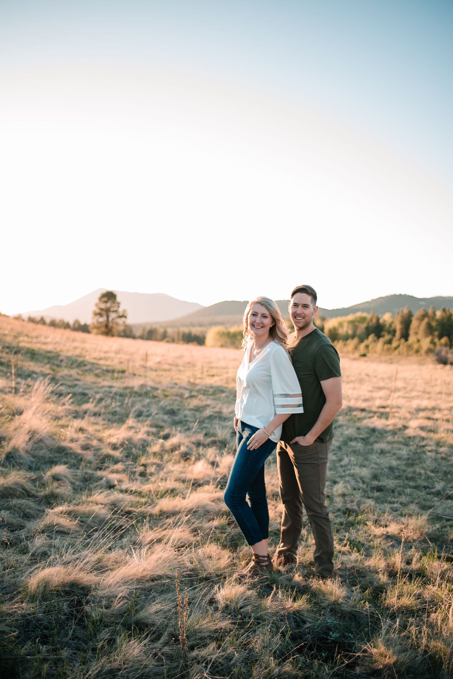 A couple shares a tender moment together on a grassy hillside at sunset.