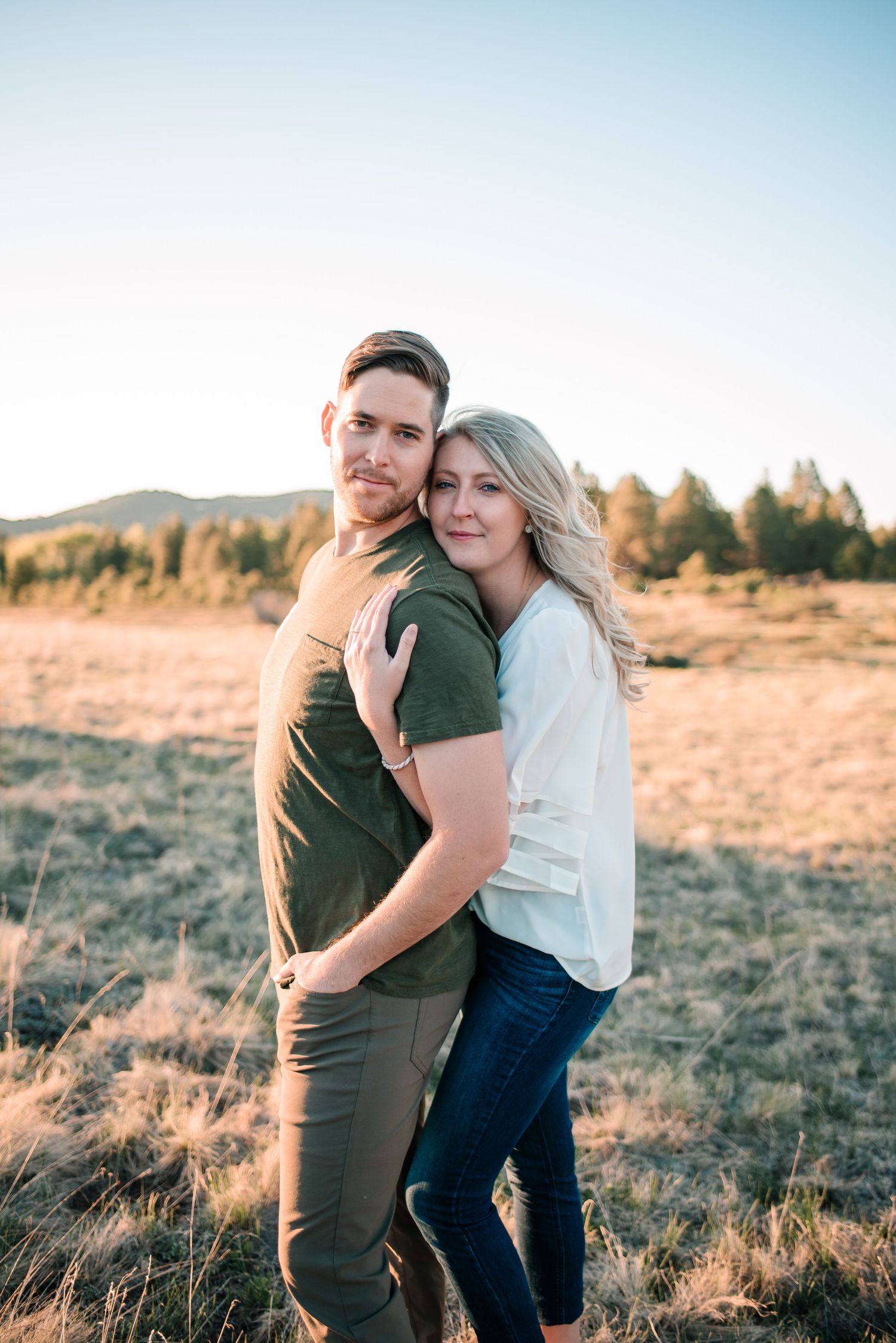 Two people embrace lovingly in a golden field during sunset.