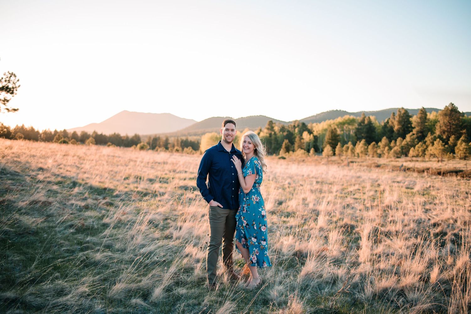 Romantic couple moment in golden field with mountain landscape at sunset.