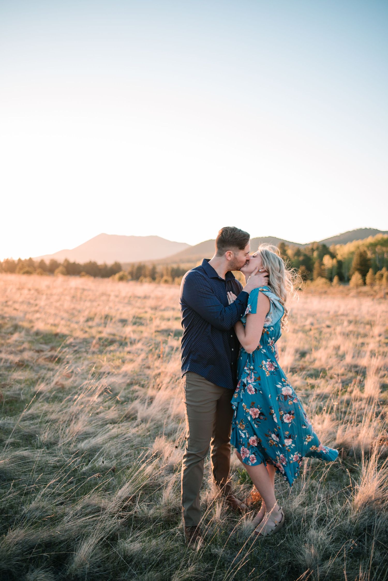 Intimate moment between couple in flowing grass field during golden hour.