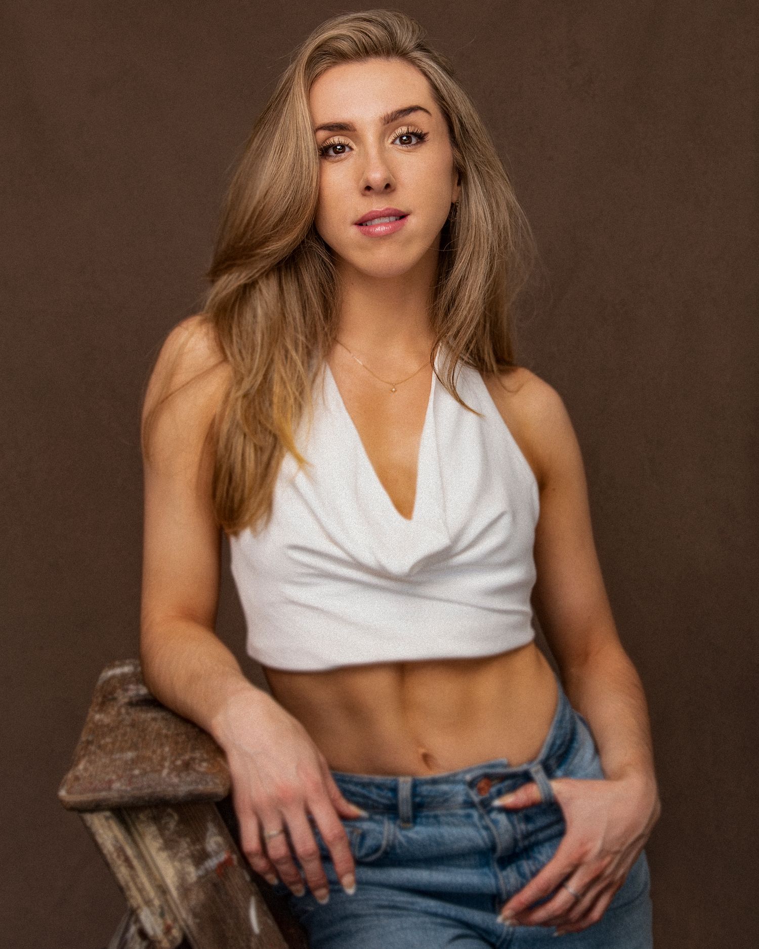 Studio portrait featuring white crop top and jeans against brown background.