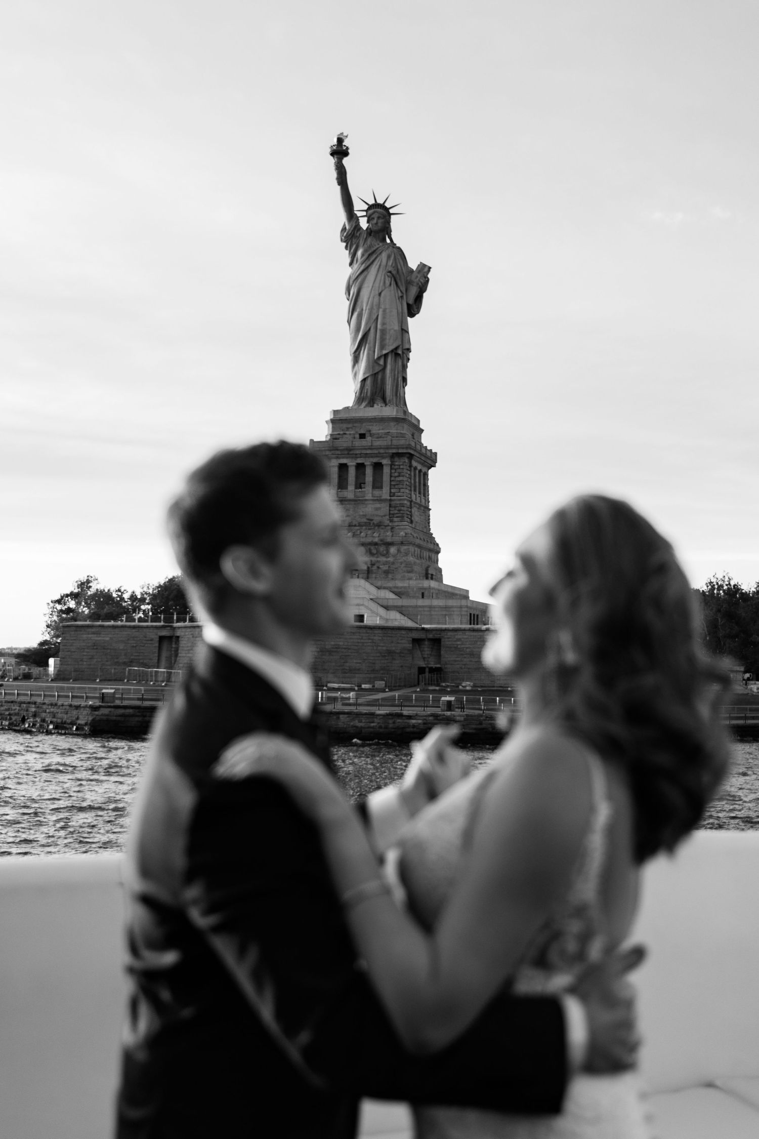 Wedding photos with Statue of Liberty silhouetted in background across New York Harbor.