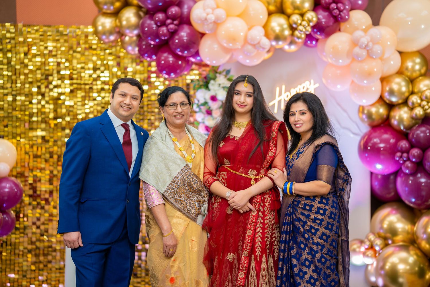 Group photo at celebration event with gold sequin wall and pink and gold balloon decorations.
