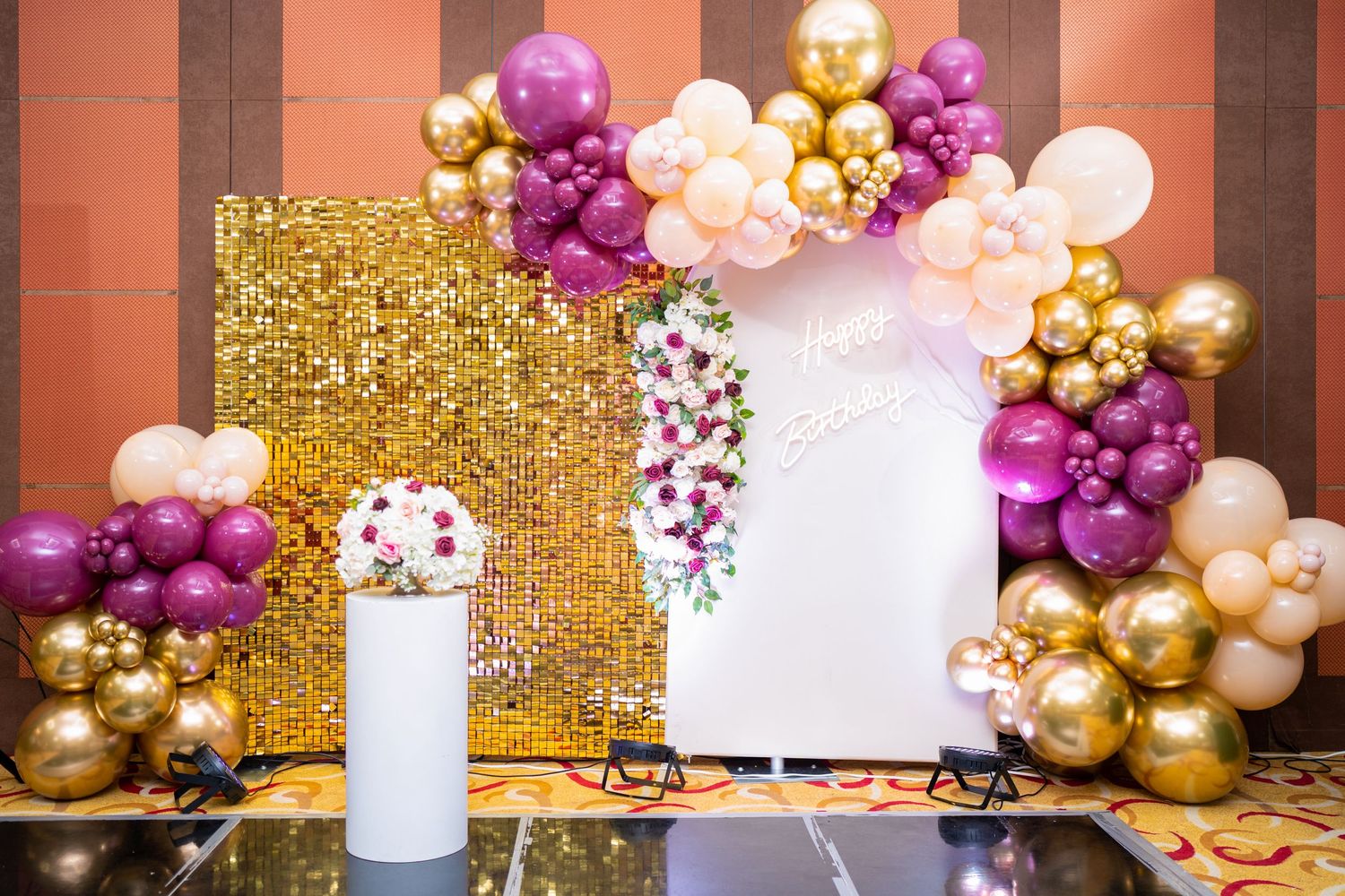 An elegant event backdrop with gold sequins and purple and gold balloon arch decorations.