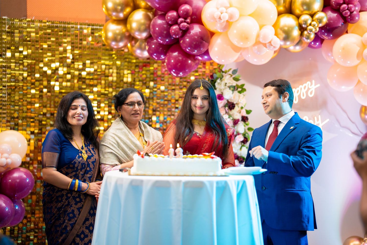 Birthday cake cutting moment at celebration with gold sequin backdrop and balloons.