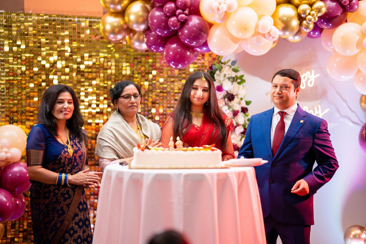 A celebration event with decorative balloons and flowers featuring a table setup against a golden backdrop.