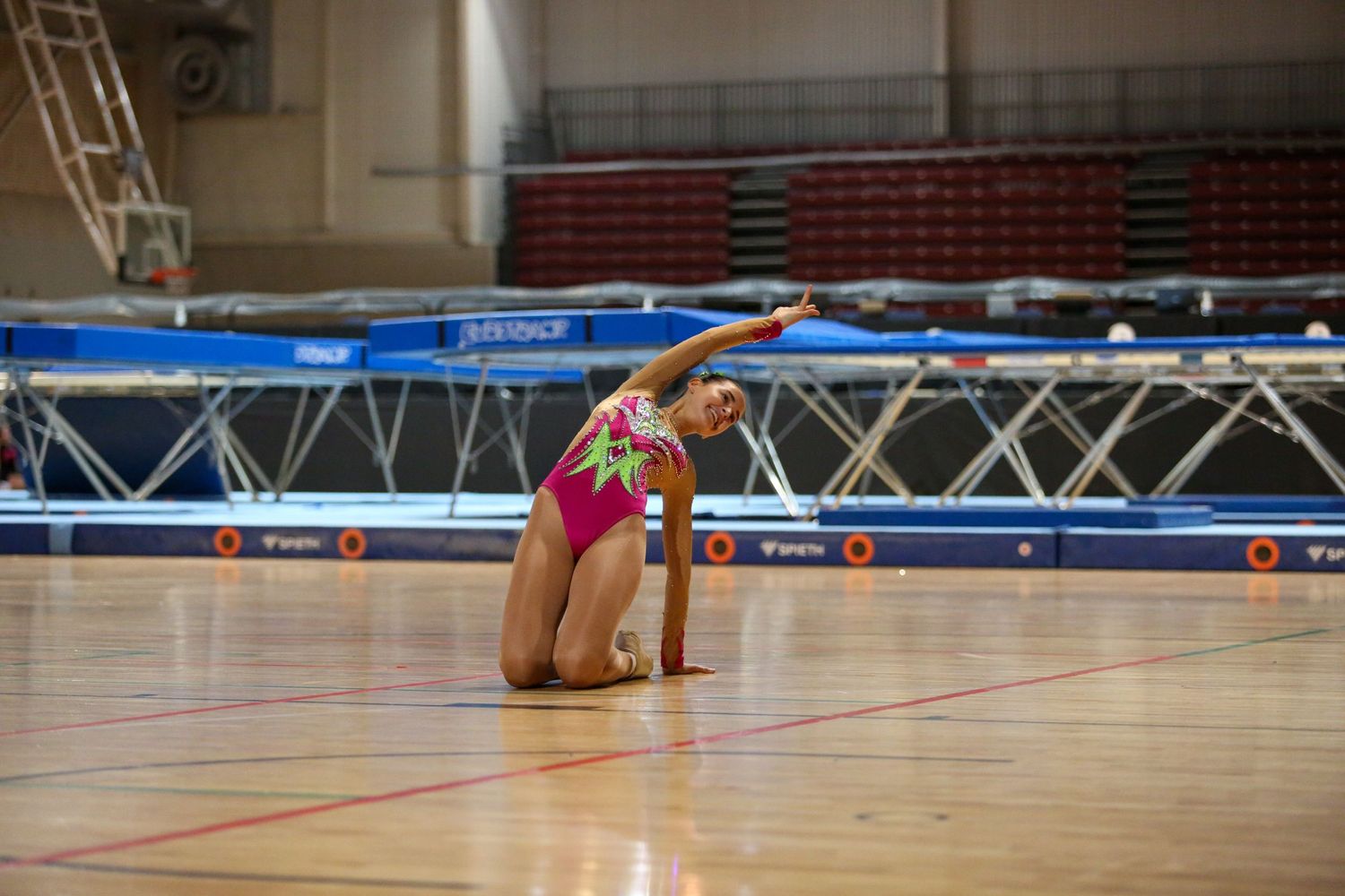 Trampoline athlete performs backbend move during indoor competition routine.