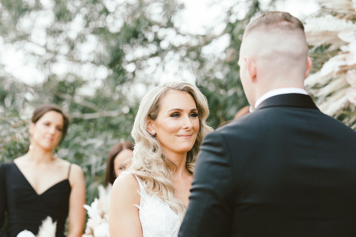 Couple exchanging emotional vows during an outdoor wedding ceremony beneath leafy trees.