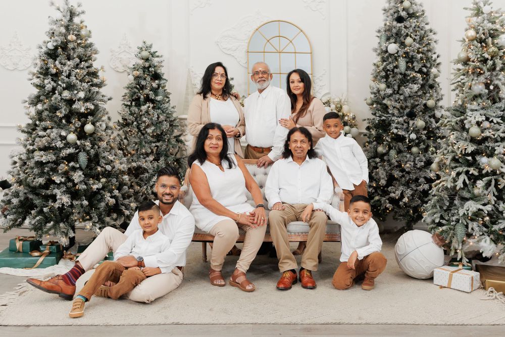 A family group in coordinated white outfits poses together on a bench with Christmas trees in the background.
