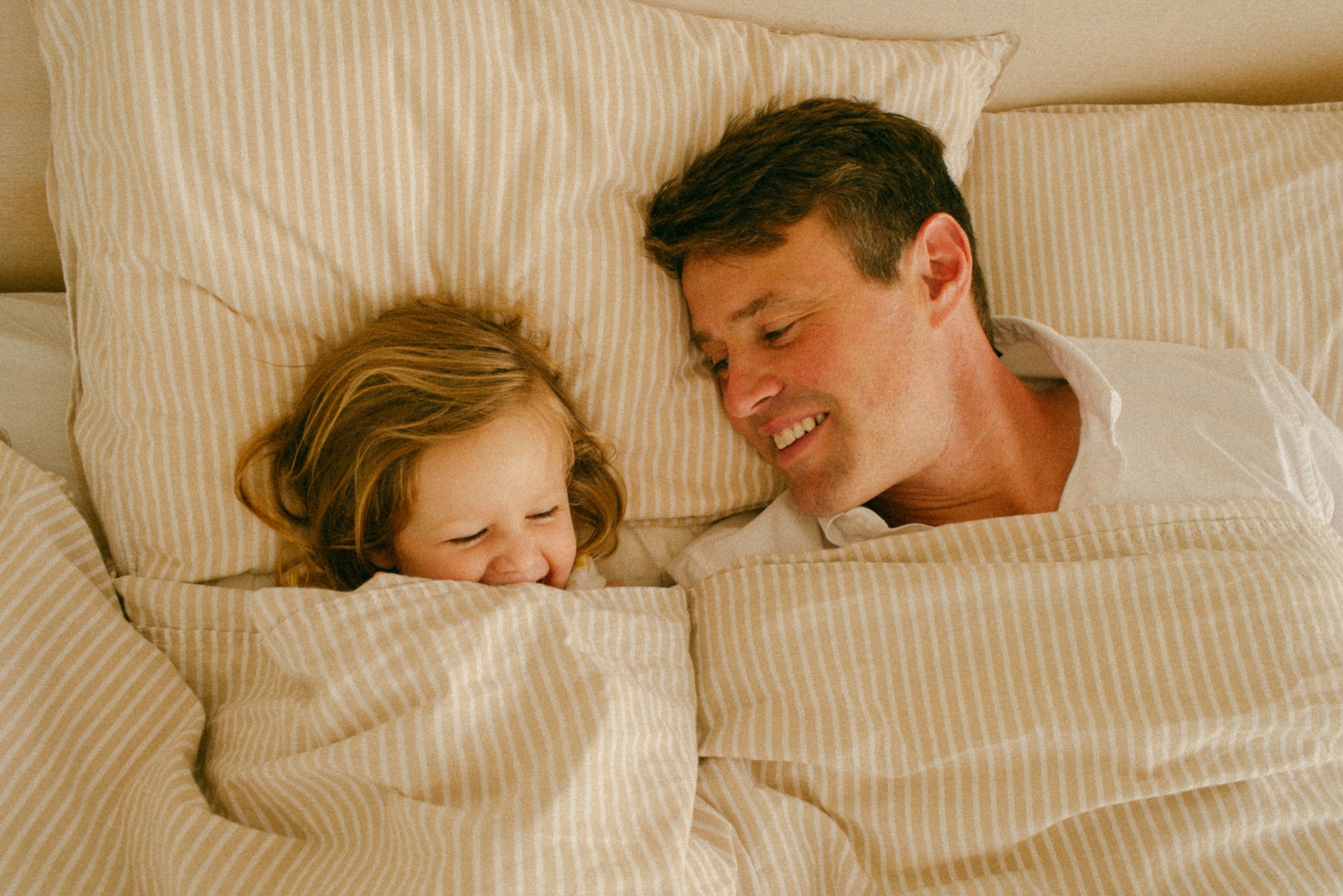 Heartfelt maternity session in Sydney & Northern Beaches, with dad and daughter sharing playful moments on the bed, celebrating family love