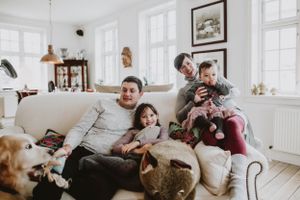 Family playing and talking on the couch with their dog, photographed indoors in natural light, highlighting authentic, joyful moments.