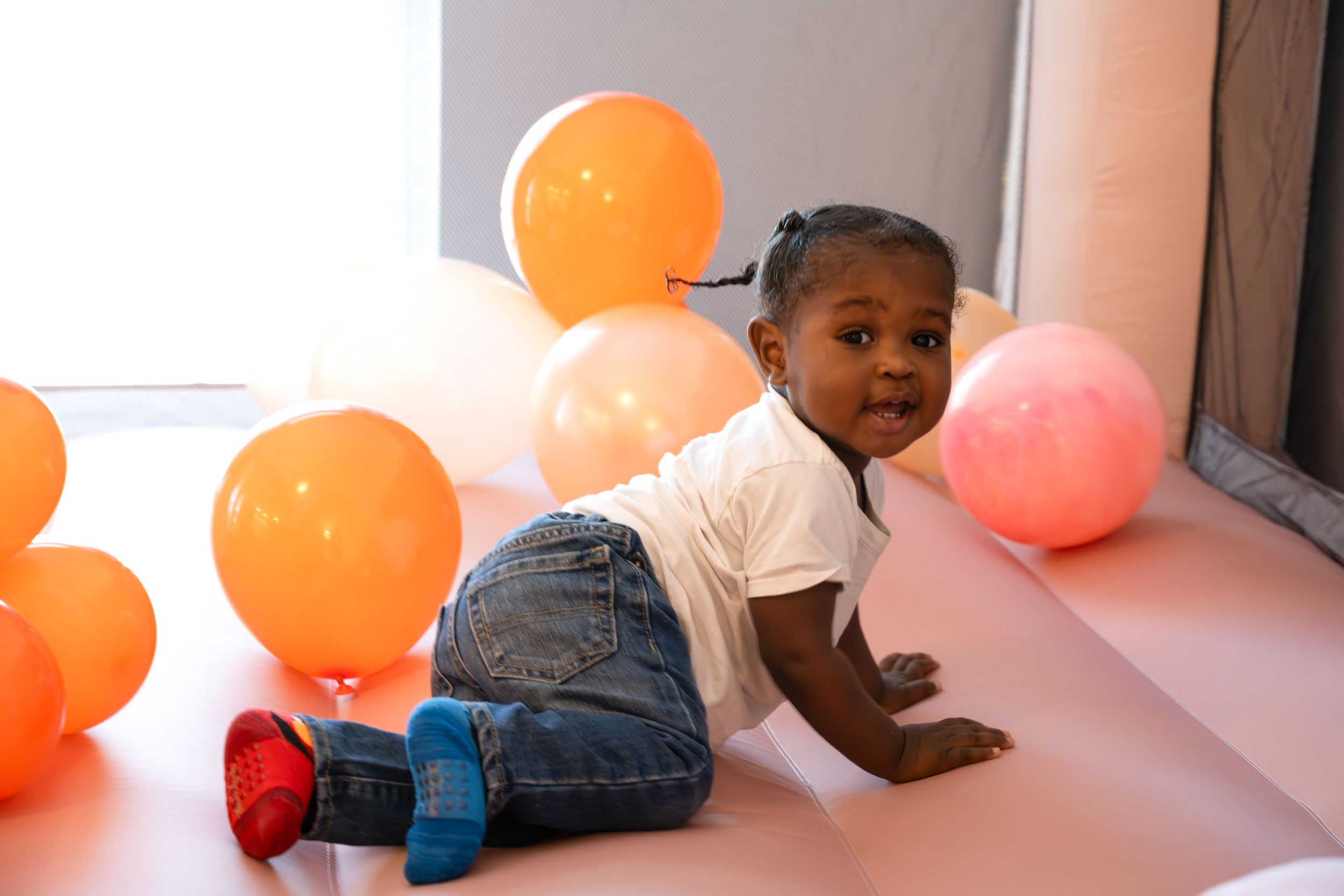 Small child crawling near orange balloons in natural light setting.
