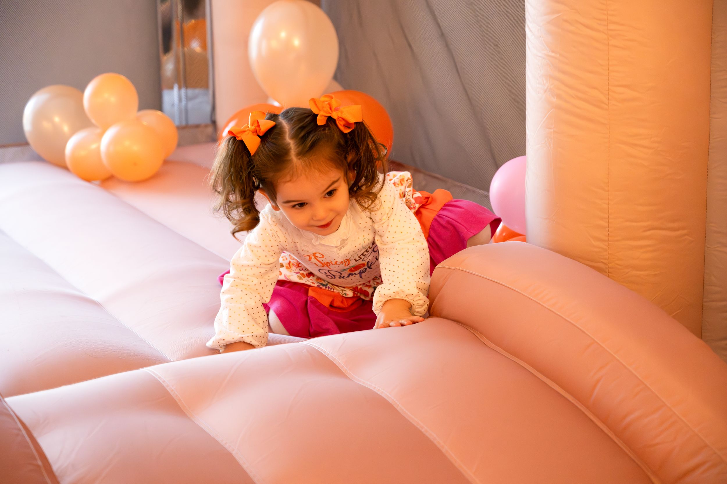 Child crawling and playing on pink inflatable bouncy surface.
