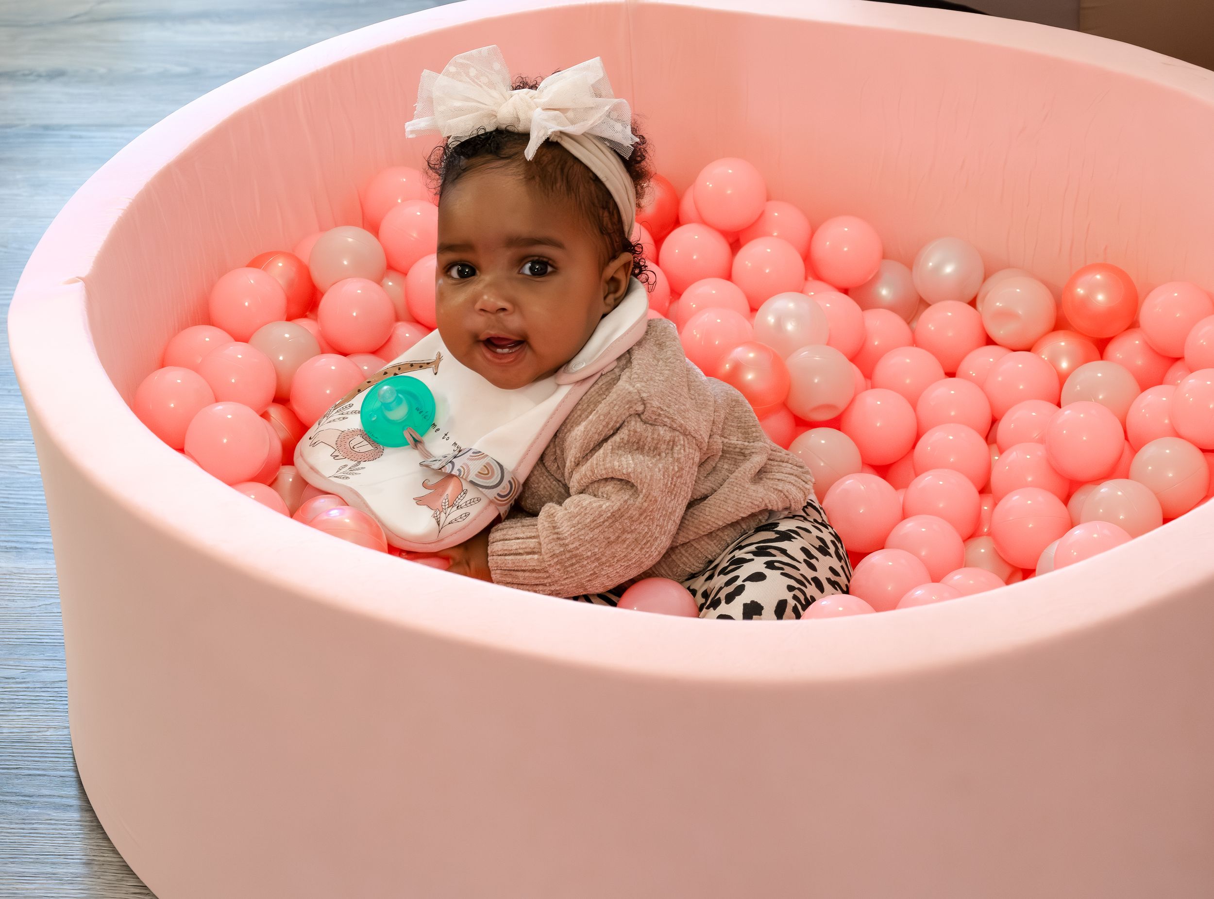 Small child sitting in pink ball pit filled with coral and white balls.