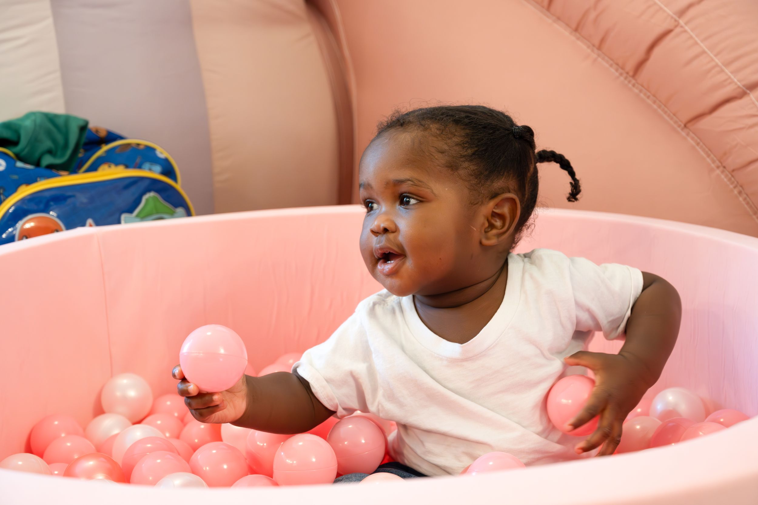 Excited child playing and laughing in pink ball pit.