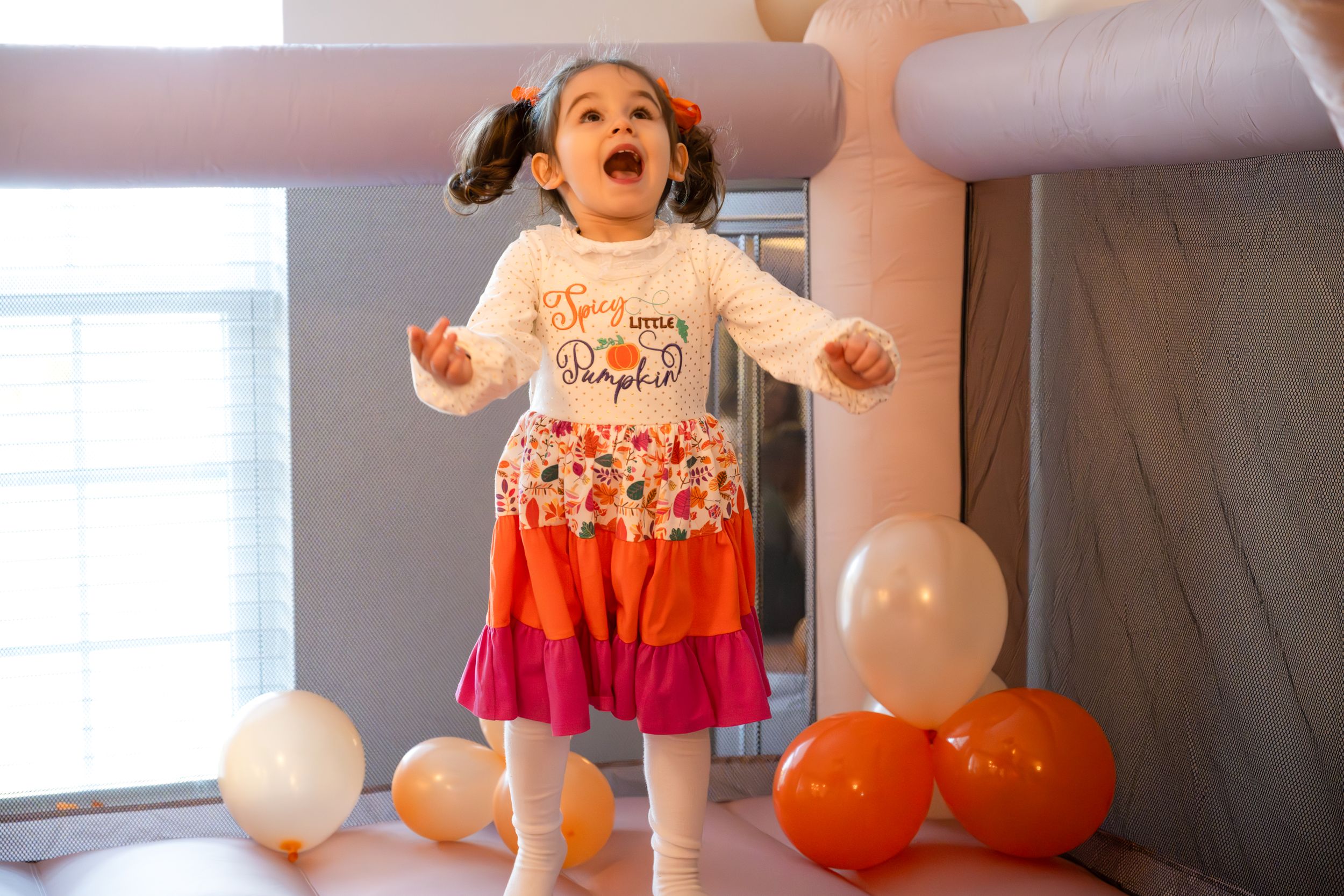 Excited child jumping with joy among orange and white balloons at a party celebration.