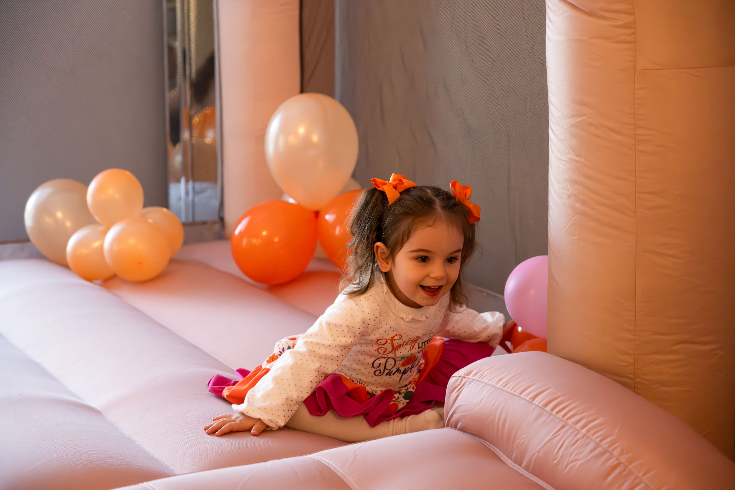 Child having fun on pink bounce house with orange balloons in background.