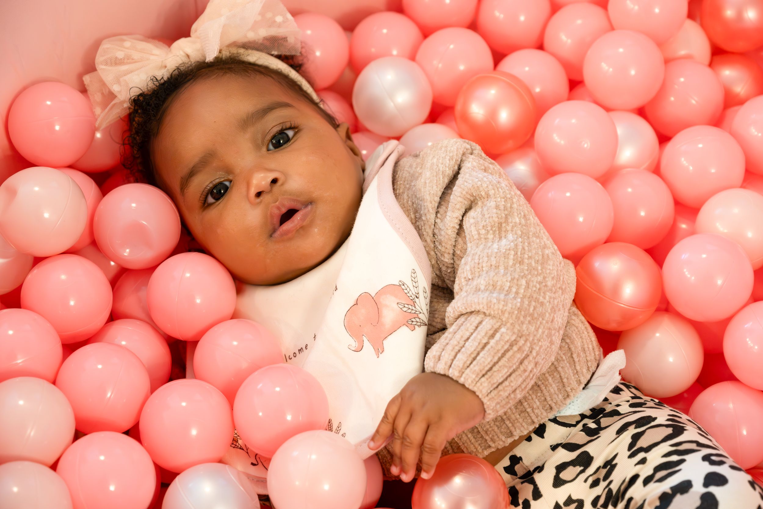 Baby in animal print outfit playing in pink ball pit.