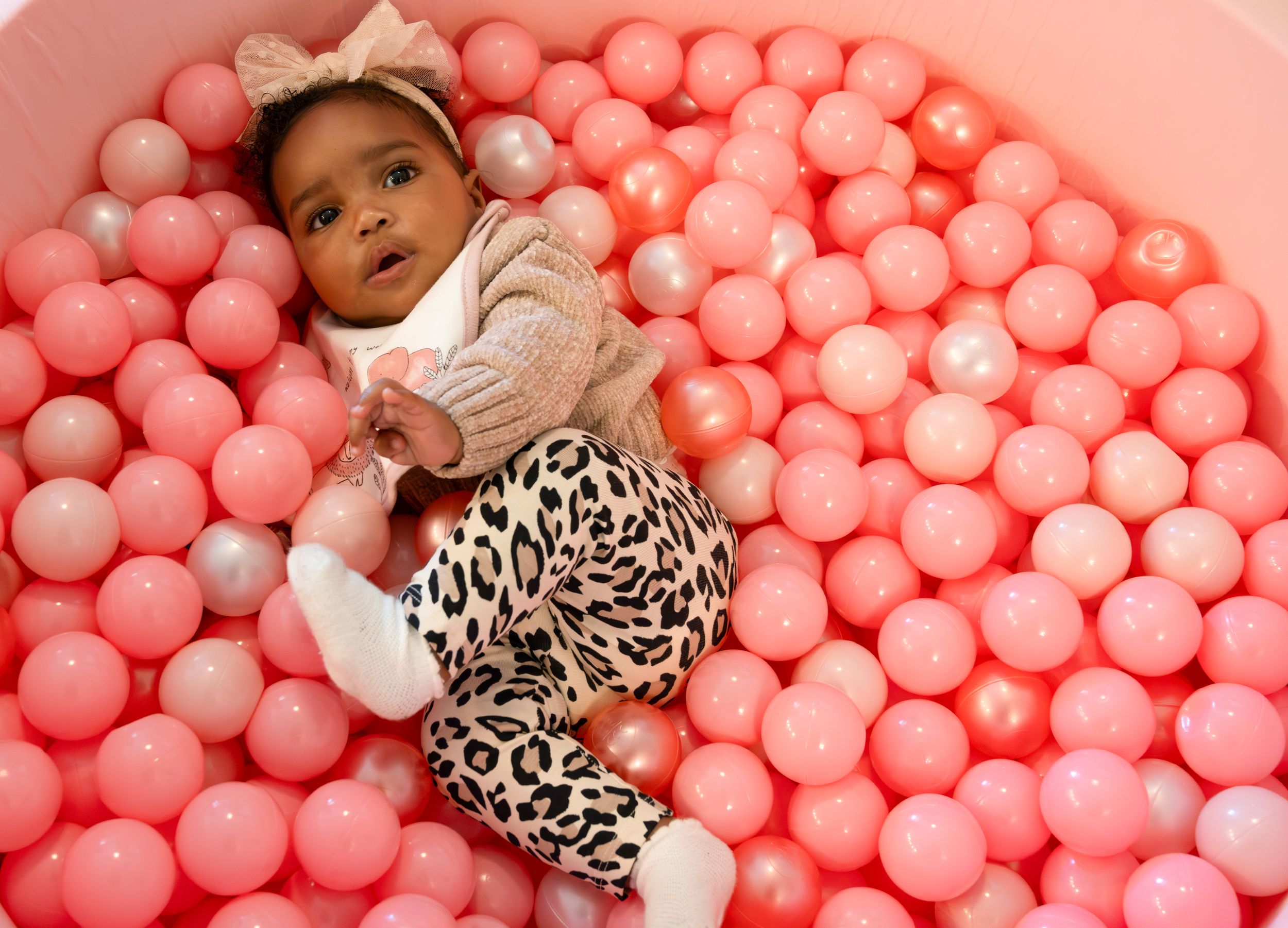 Playful baby in beige sweater enjoying pink ball pit.