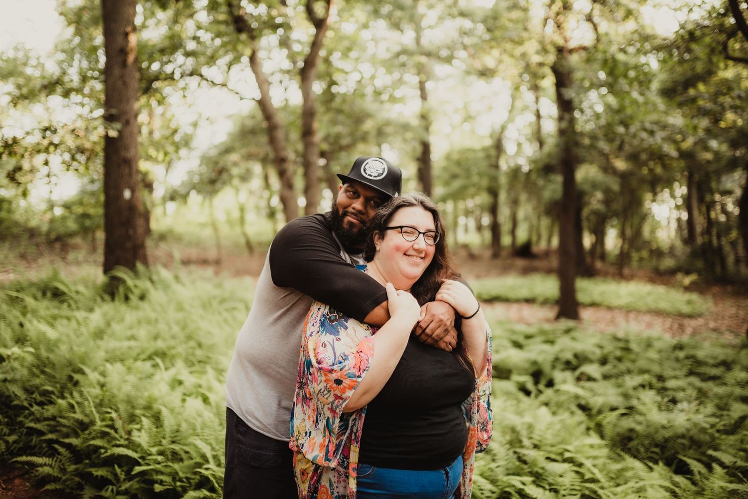 two lovers stand hugging in the woods, a field of ferns is in the background