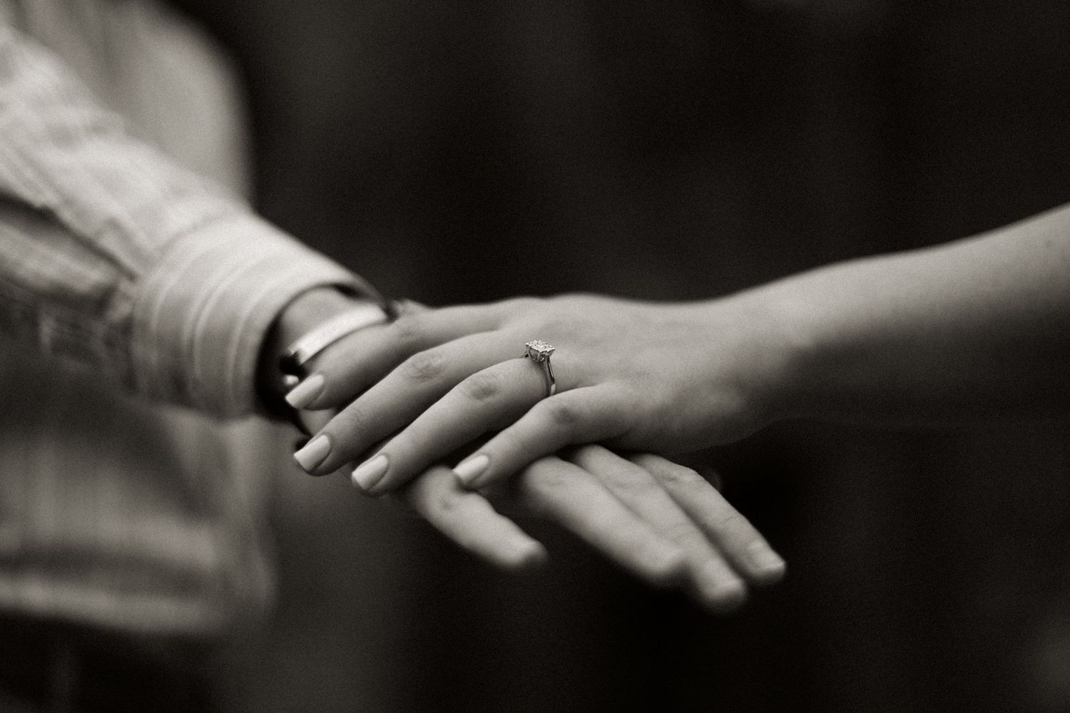 Close-up black and white photo of hands wearing wedding rings in tender moment.