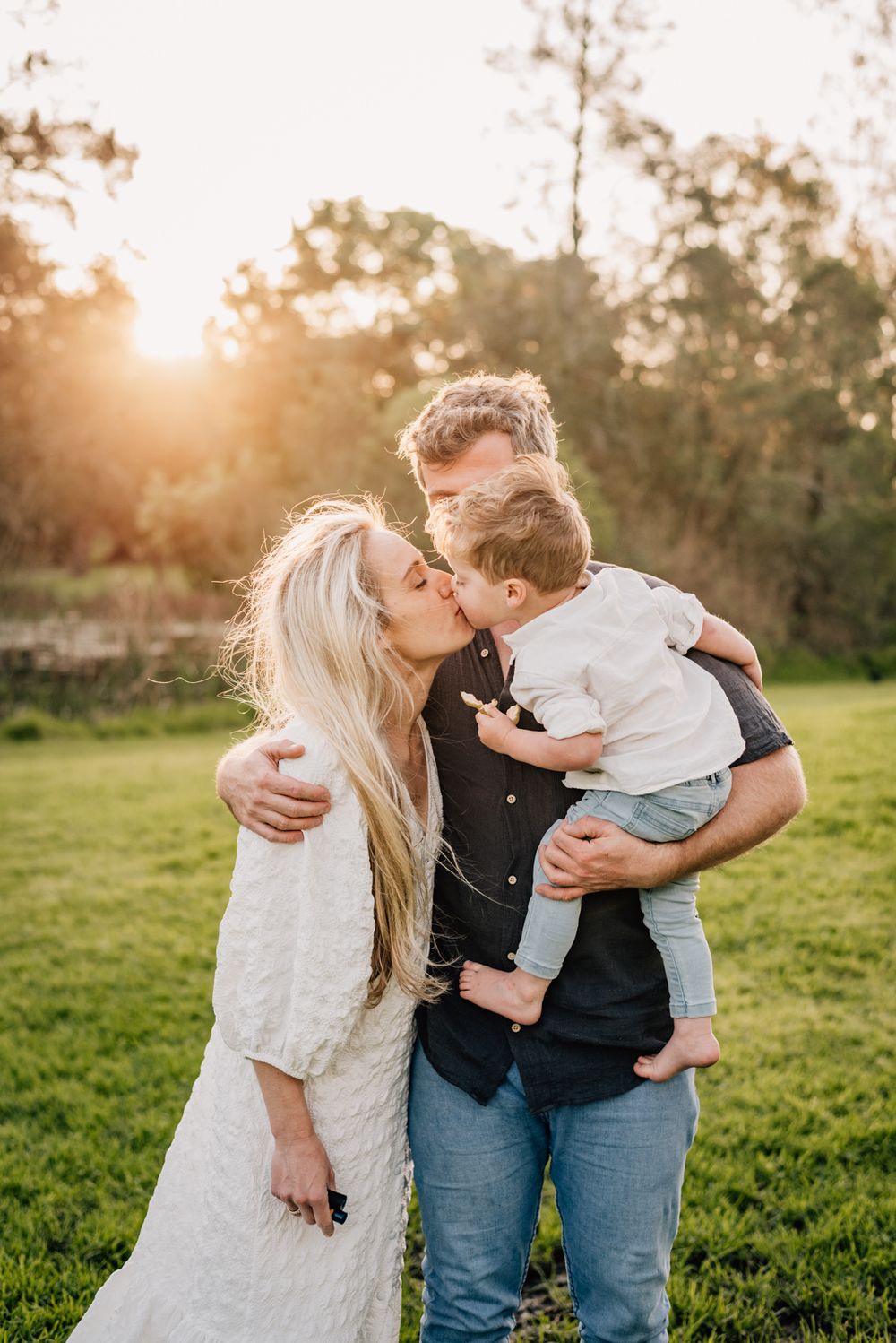 Intimate family moment captured during sunset in grassy field.