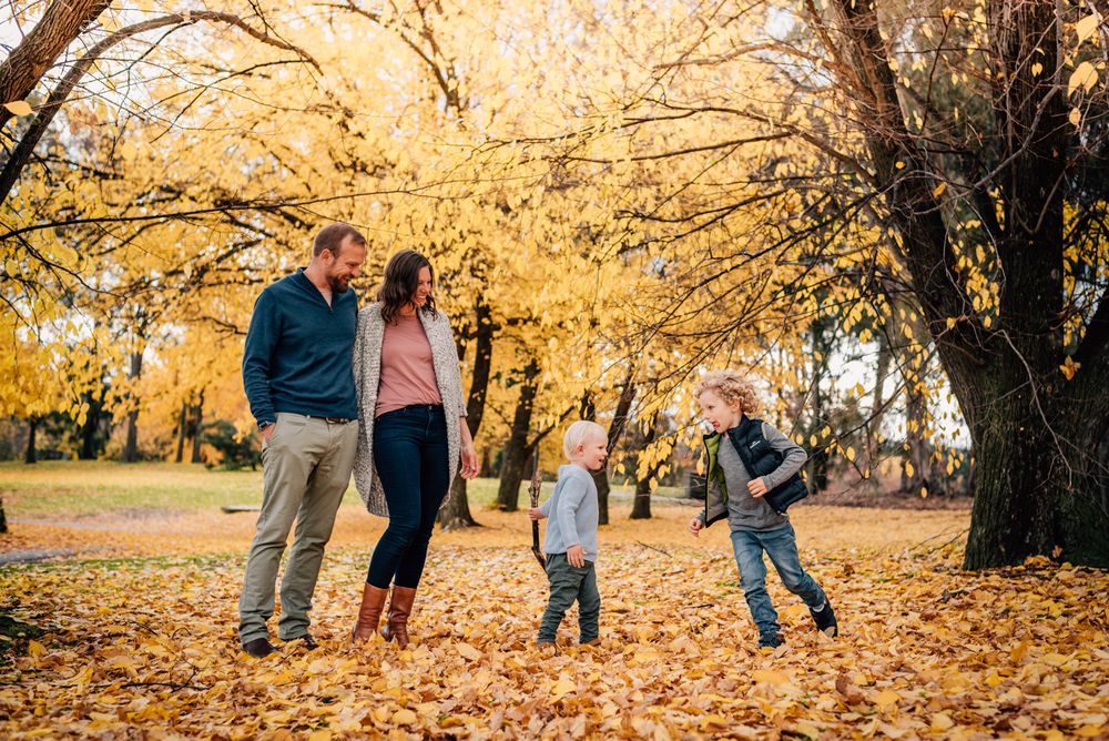Family enjoying a bright autumn day together under golden trees with fallen leaves.
