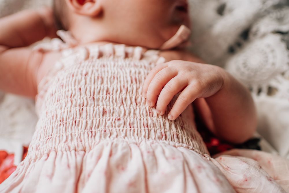 Close-up detail of baby wearing pink smocked dress while resting.
