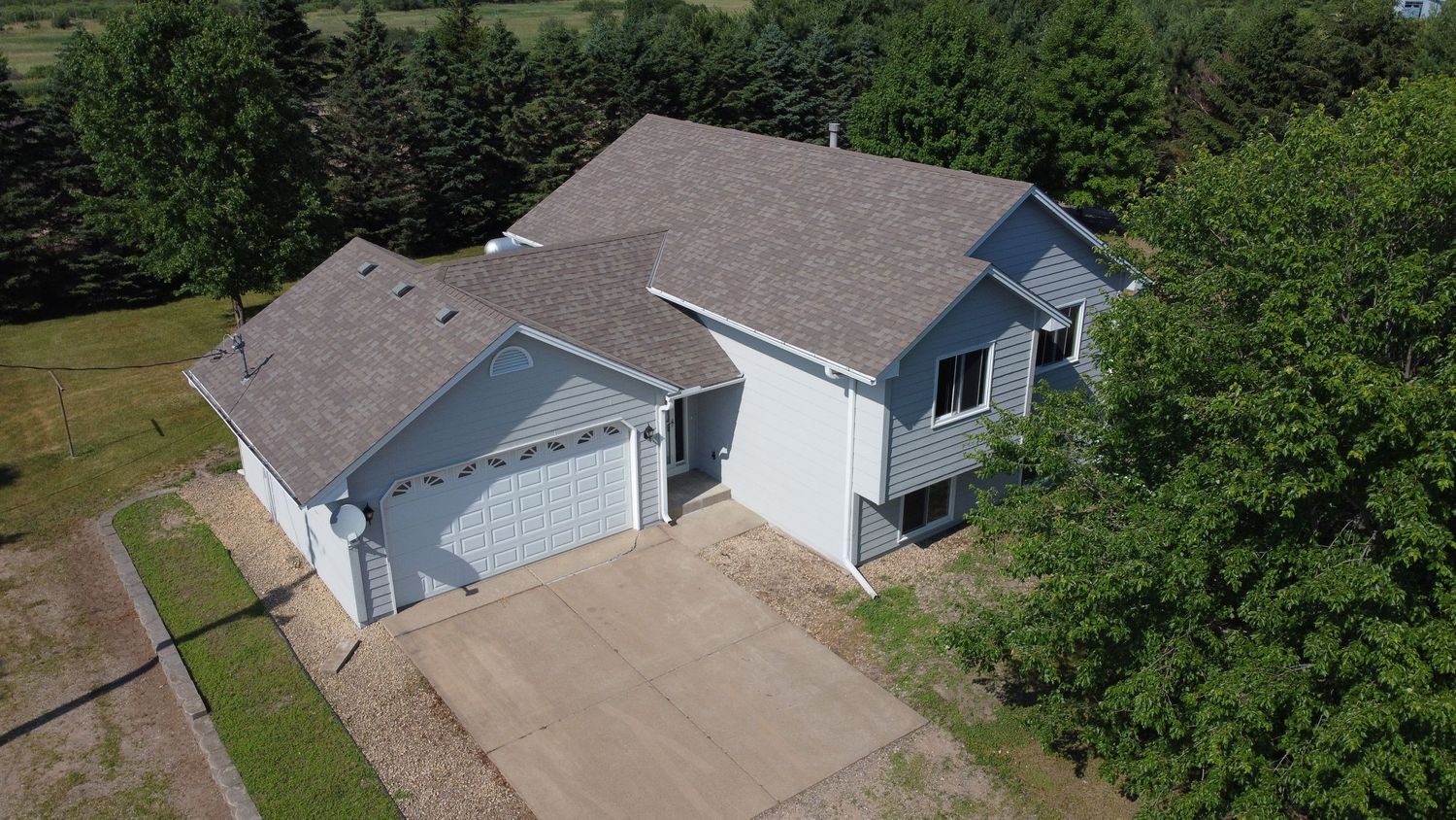 Aerial view of a white split-level home with attached garage and driveway surrounded by trees.